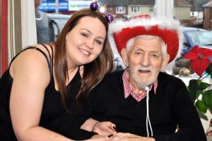 A resident wearing a Santa cowboy hat smiling to the camera with his granddaughter